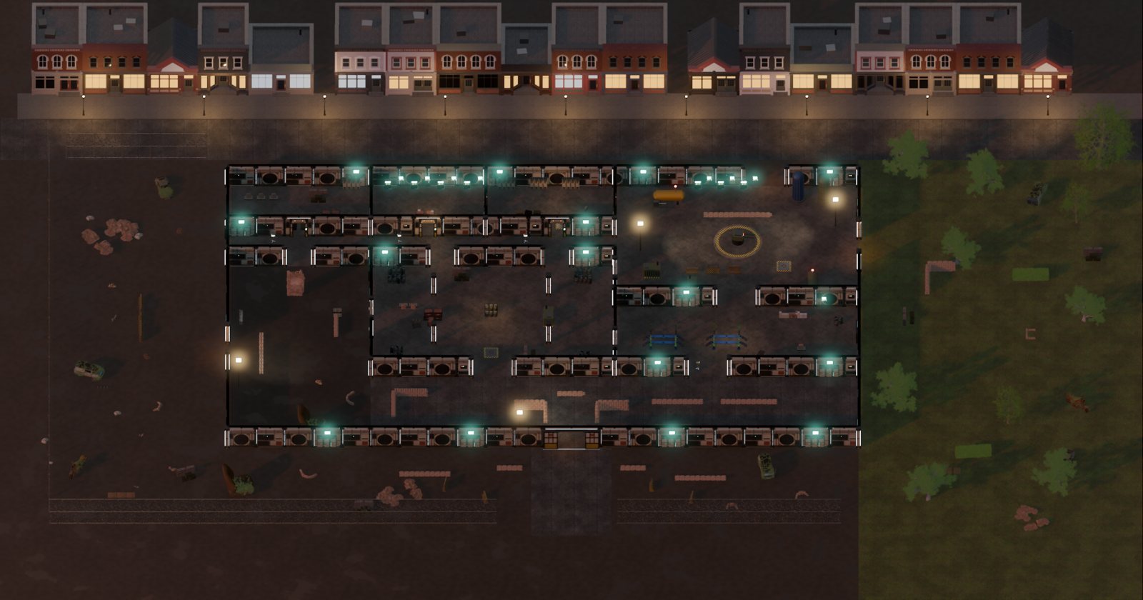 A walled military compound at dusk with lit wall strips, a town's shopfronts along the top edge and grass to the east